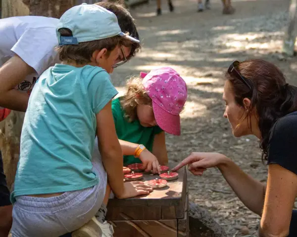 Une famille résout une énigme pour course d'orientation, manipulant des jetons sur un jeu en bois.