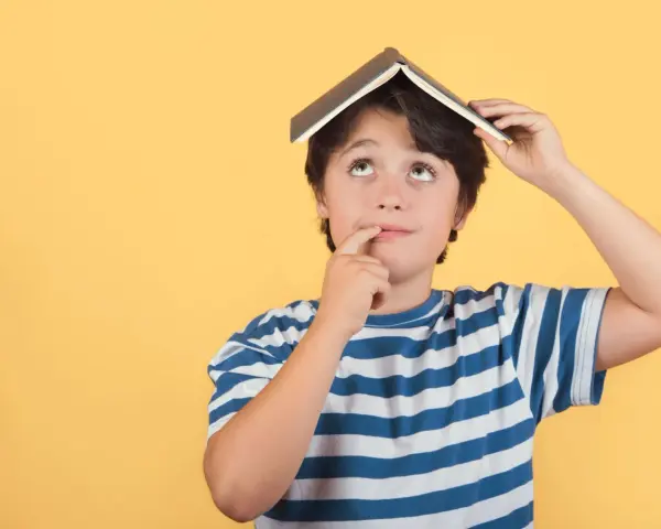Un enfant de 5 ans, avec un livre sur la tête, réfléchit. Il est en colonie de vacances.