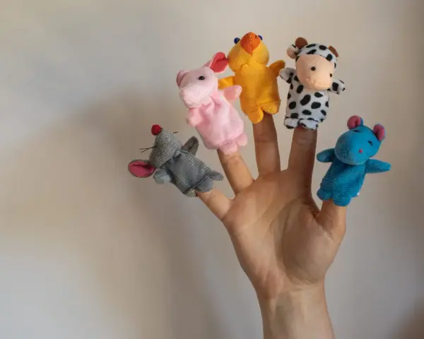 Main d'une personne avec cinq marionnettes à doigts en feutrine : souris grise, lapin rose, canard jaune, vache noire et blanche, hippocampe bleu.