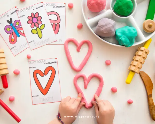 Pâte à modeler rose en forme de cœur, cartes d'activités, rouleaux et petites boules de pâte.