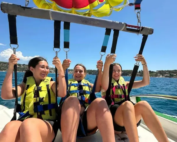 Trois jeunes femmes souriantes en parachute ascensionnel au-dessus de la mer.