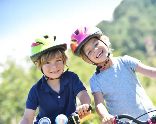 Deux enfants souriants, casques de vélo colorés, profitent de leurs vacances scolaires en Savoie.