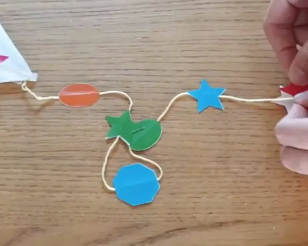 Fabrication d'un cerf-volant étoile : fils, formes colorées (étoiles, ovales, octogone) et mains.