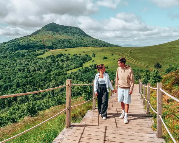 Couple marchant sur un chemin en bois avec un volcan en arrière-plan en Auvergne.