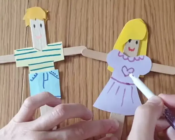 Poupées en bâtonnets de bois, une fille et un garçon, décorées par des mains d'enfant.