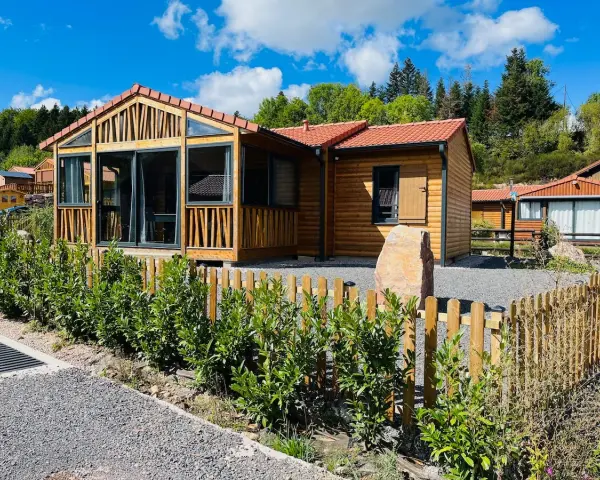 Chalets en bois avec clôture et végétation devant, sous un ciel bleu.