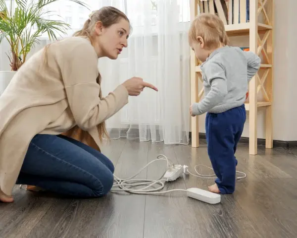 Une femme réprimande un enfant près de prises électriques au sol.