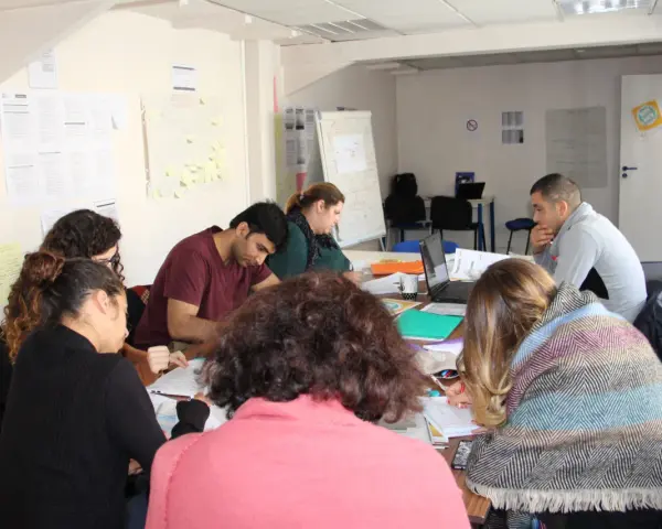 Groupe de personnes assises autour d'une table, travaillant sur des documents et un ordinateur portable.