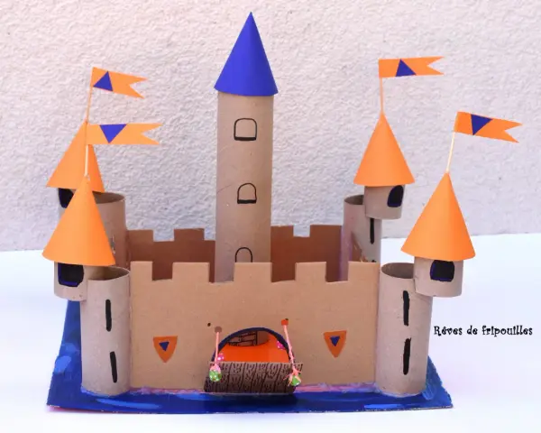 Château fort en carton avec tours, drapeaux orange et bleus, et une herse.