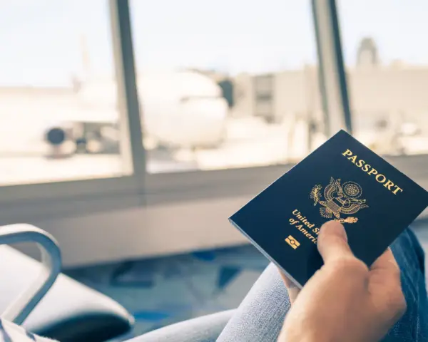 Main tenant une carte d'identité américaine devant une fenêtre d'aéroport avec un avion en arrière-plan.