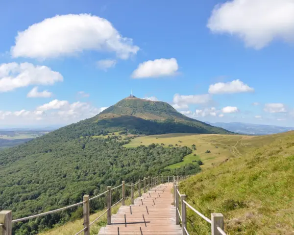 Escalier en bois menant au Puy de Dôme sous un ciel bleu et nuageux.