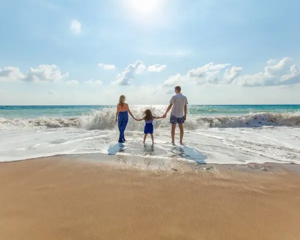 Une famille se tient la main sur la plage, profitant des vagues. Ils pensent à devenir famille d'accueil pour les vacances, offrant ces moments de bonheur.