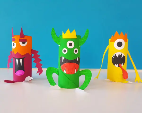 Trois monstres colorés faits à la main, en rouleaux de papier toilette, sur fond bleu.