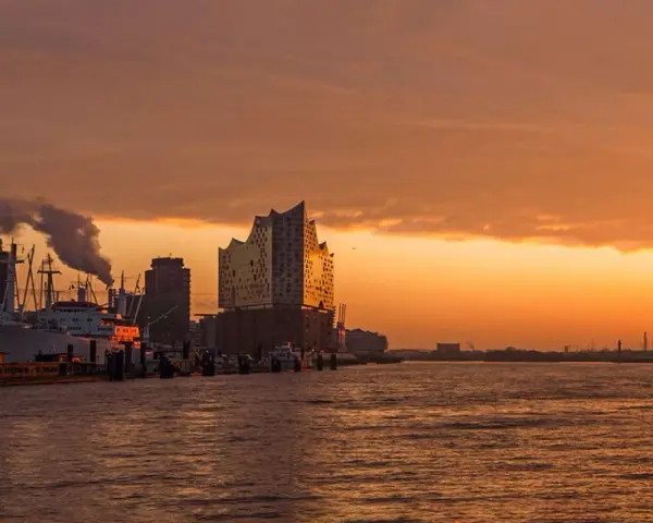 Coucher de soleil sur le port de Hambourg, idéal pour visiter Hambourg en 3 jours. Bateaux, grues et la Philharmonie de l'Elbe se reflètent sur l'eau.