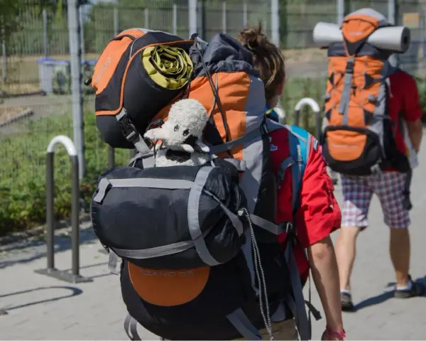 Deux jeunes partent en camp de scout, chargés de leurs sacs à dos. Un doudou mouton est accroché au sac de devant.