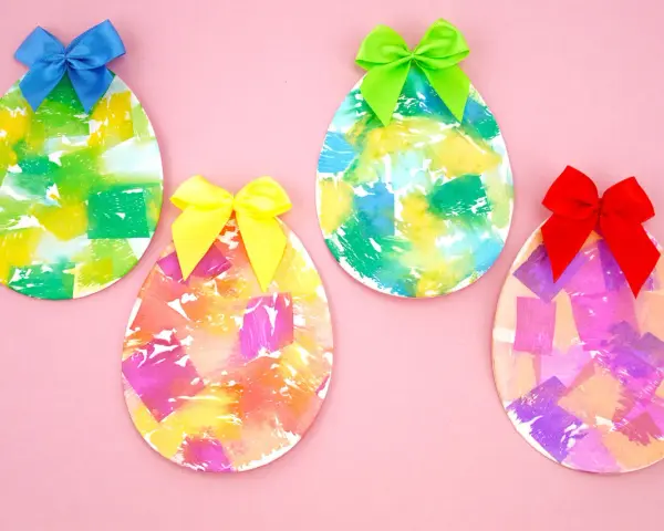 Quatre œufs décorés de papier crépon coloré et ornés de rubans sur fond rose.