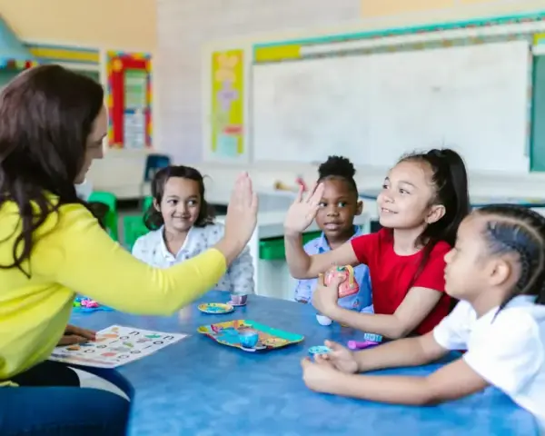 Une enseignante donne une tape dans la main à des enfants autour d'une table dans une salle de classe.