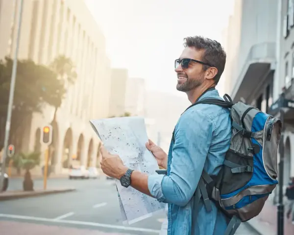 Un homme souriant avec un sac à dos consulte une carte, prêt pour un voyage en immersion dans la ville.