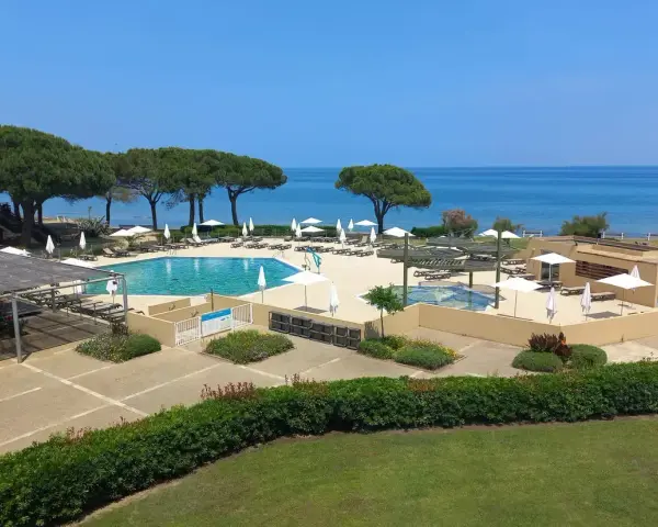 Piscine et transats dans un complexe hôtelier en bord de mer, sous un ciel bleu.