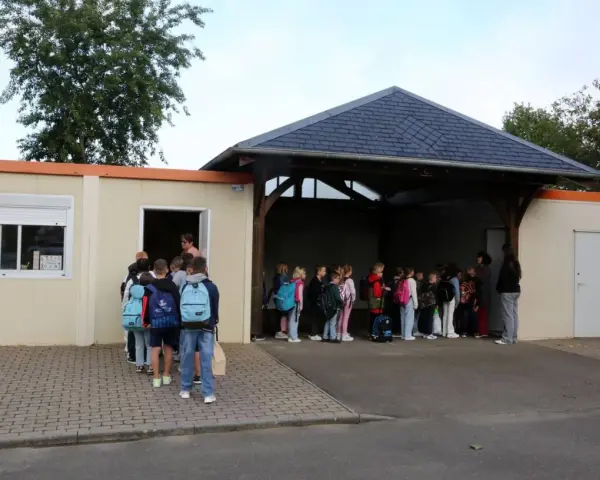 Des enfants font la queue devant un bâtiment scolaire, certains avec des sacs à dos.