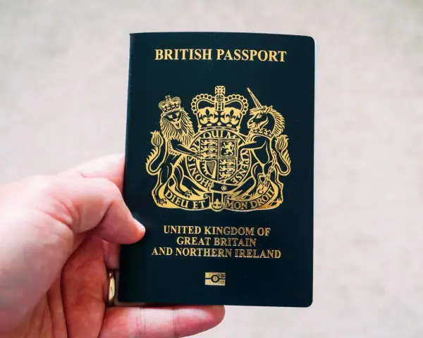 Main d'une personne tenant un passeport britannique bleu foncé avec le blason royal doré.