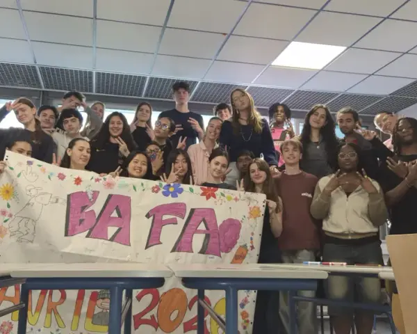 Un groupe d'étudiants pose derrière une banderole "BAFA" décorée de dessins et de fleurs.