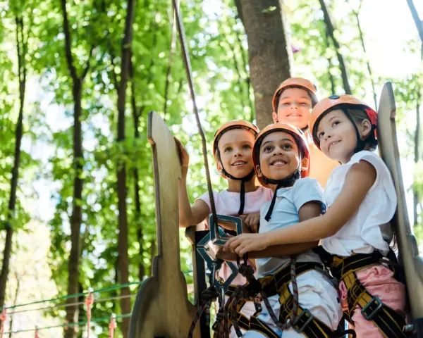 Quatre enfants souriants portant des casques de sécurité dans un parc d'aventure.