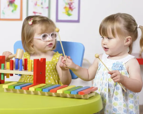 Deux petites filles s'amusent avec un xylophone, explorant la musique et les activités manuelles.