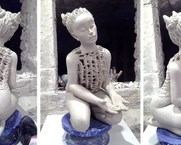 Sculpture en argile d'une jeune fille aux cornes, assise, vêtue d'une tunique ajourée.