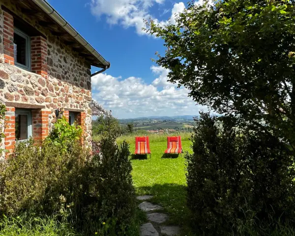 Maison en pierre avec vue panoramique sur les collines, deux chaises longues rouges invitent à la détente. Parfait pour découvrir les destinations Rhône-Alpes.