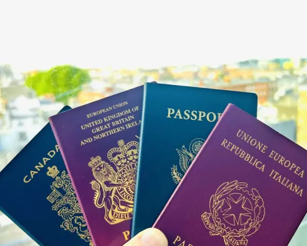Plusieurs passeports (Canada, Royaume-Uni, UE, Italie) tenus devant un paysage urbain flou.