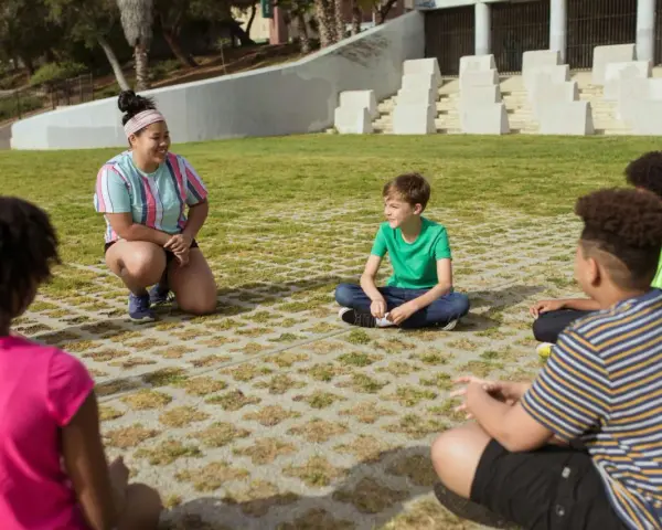 Une animatrice discute avec des enfants assis en cercle dans un parc.