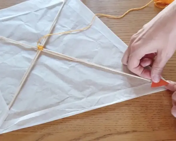 Mains fabriquant un cerf-volant en papier blanc avec des bâtons de bois et de la ficelle.
