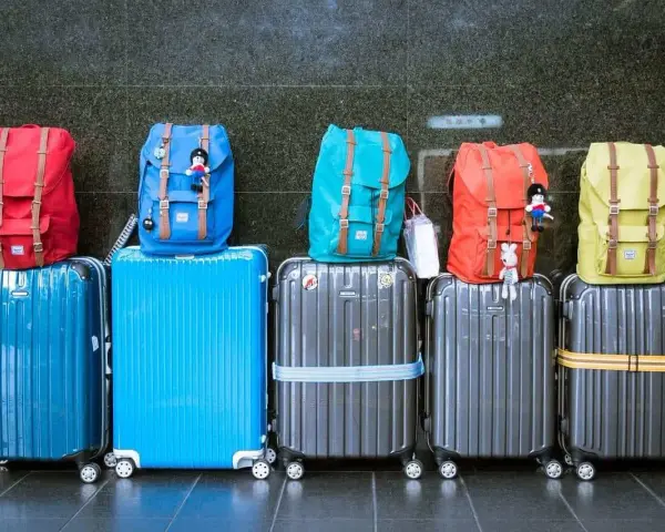 Six valises de différentes couleurs empilées, avec des sacs à dos colorés sur le dessus.