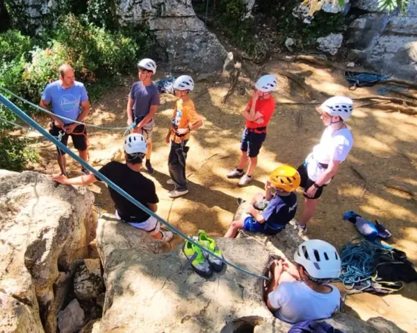 Des jeunes en pleine colonie de vacances escalade, casques blancs et jaunes, prêts pour l'aventure sur les rochers.