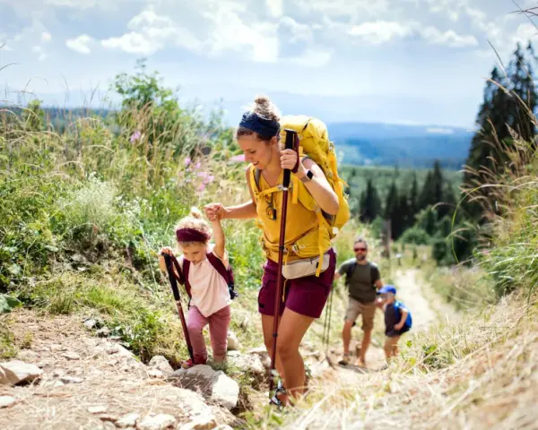Famille faisant de la randonnée en montagne, une mère aide sa fille à monter un sentier.