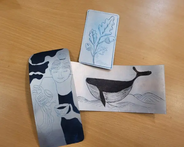 Trois gravures sur brique de lait : une femme, une baleine et une branche de chêne.