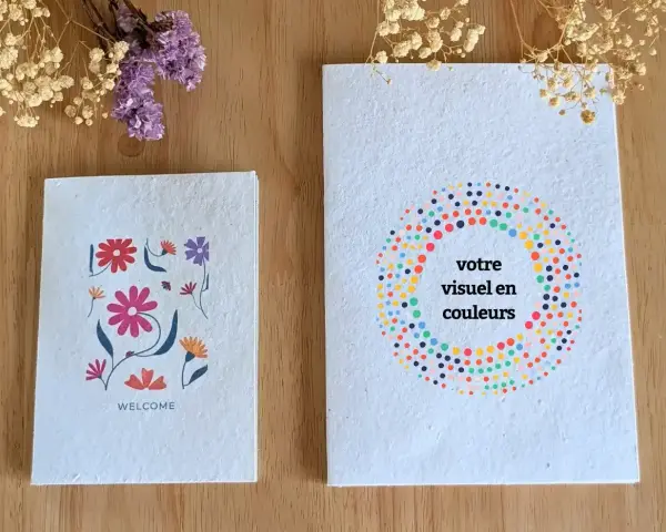 Deux carnets faits main sur fond de bois, décorés de fleurs et de points colorés.
