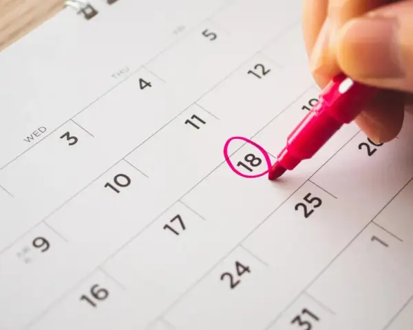 Une main entoure le 18 sur un calendrier, marquant le début des vacances scolaires à Fribourg.