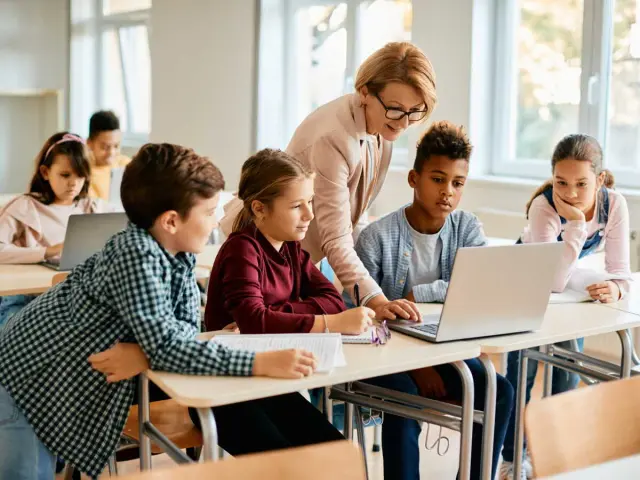 Enseignante aidant des élèves sur un projet d'accueil individualisé avec des ordinateurs en classe.