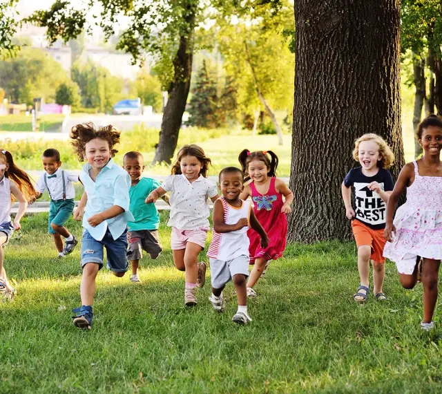 Des enfants joyeux courent dans l'herbe, profitant d'une journée ensoleillée dans une colonie de vacances 3-6 ans.