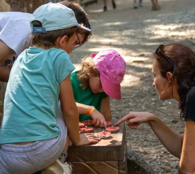 Une famille résout une énigme pour course d'orientation, manipulant des jetons sur un jeu en bois.