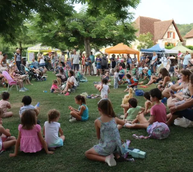 Une foule joyeuse, petits et grands, profite d'une fête de village. Une belle idée animation fête de village, avec des stands et des gens assis sur l'herbe.