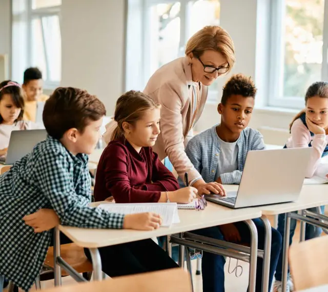 Enseignante aidant des élèves sur un projet d'accueil individualisé avec des ordinateurs en classe.