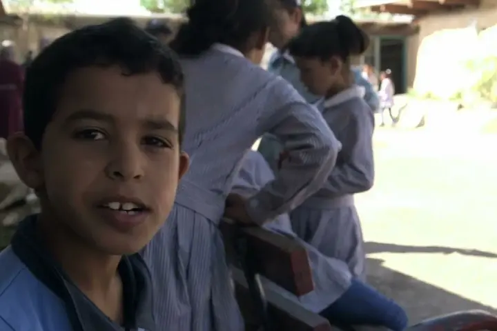 Un garçon souriant pose devant des filles en uniforme dans la même cour d'école.