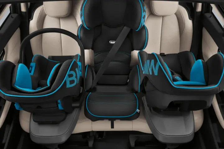 Trois sièges auto pour enfant, noir et bleu, installés sur des sièges en cuir clair. Le transport enfant en voiture est sécurisé.