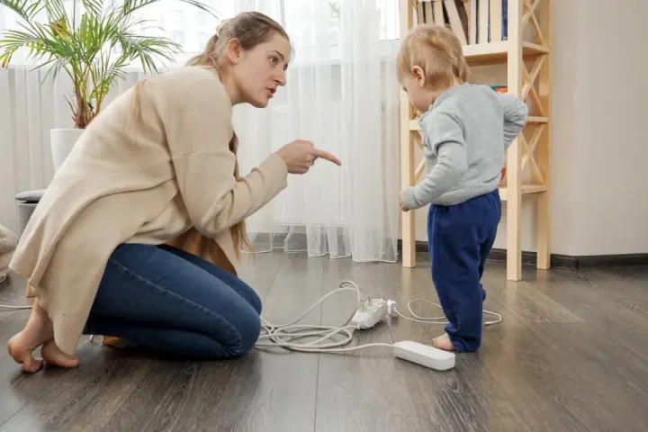 Une femme réprimande un enfant près de prises électriques au sol.