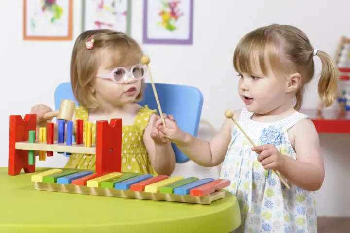 Deux petites filles s'amusent avec un xylophone, explorant la musique et les activités manuelles.