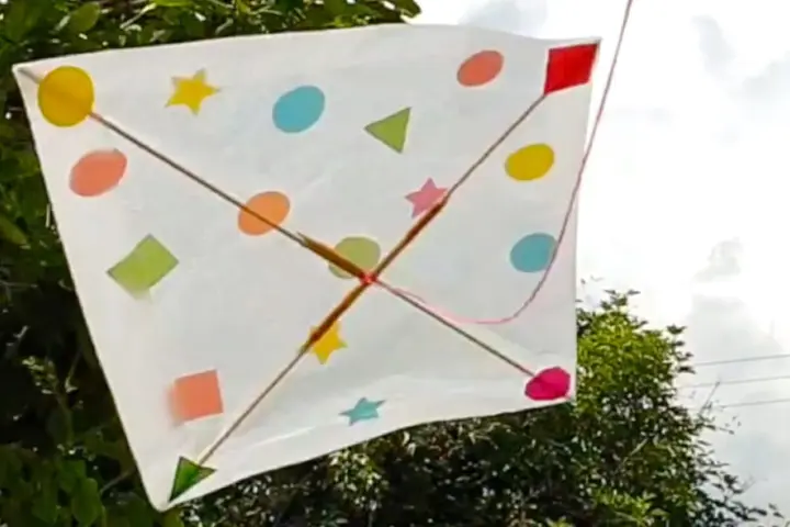 Un patron cerf-volant coloré, orné de formes géométriques et d'étoiles, flotte dans le ciel.