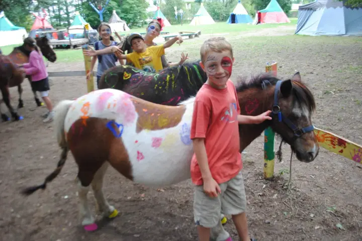 Enfants avec des poneys décorés de peinture, dans un campement avec des tentes.